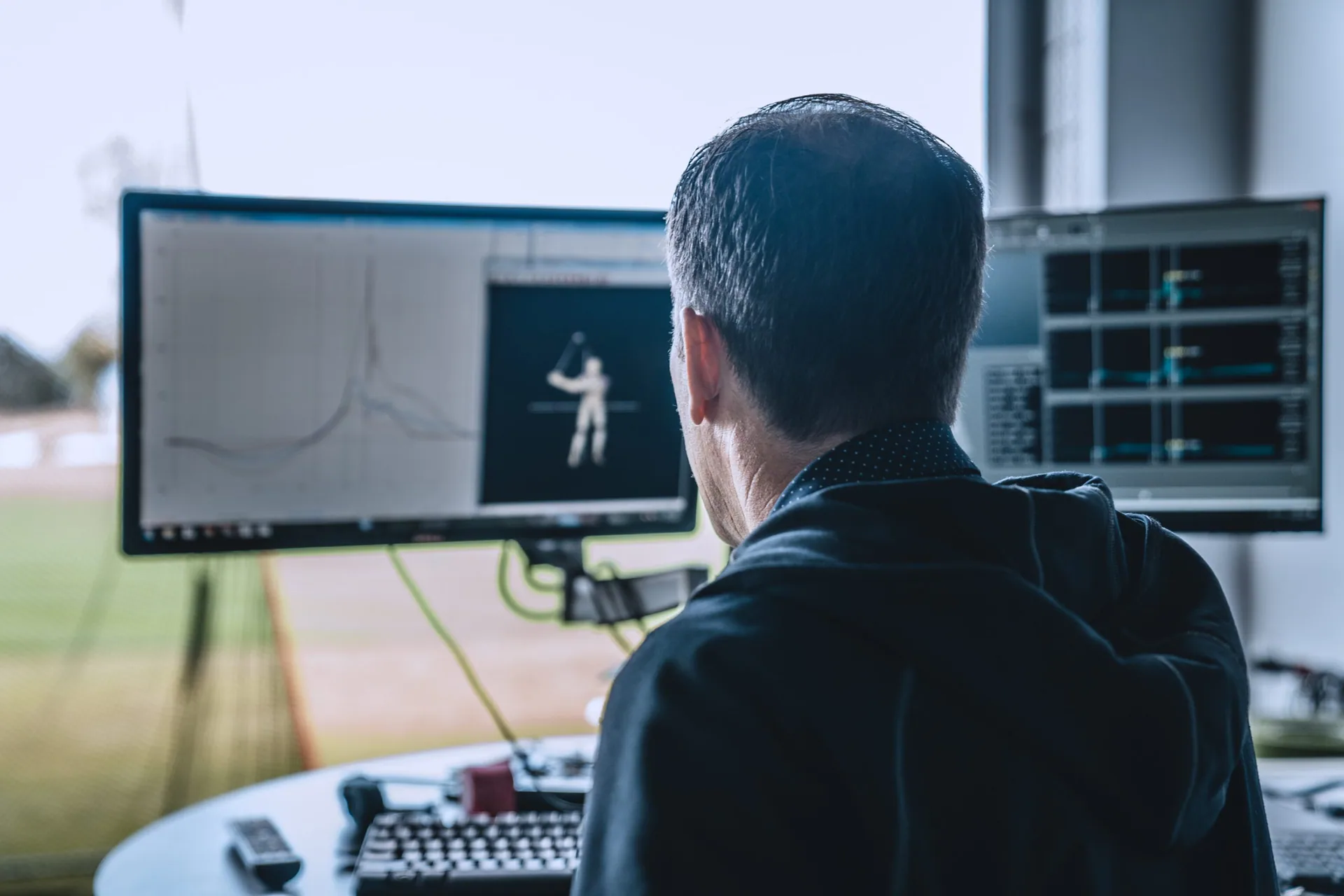 A golfer reviewing swing data on launch monitor screens in an indoor bay